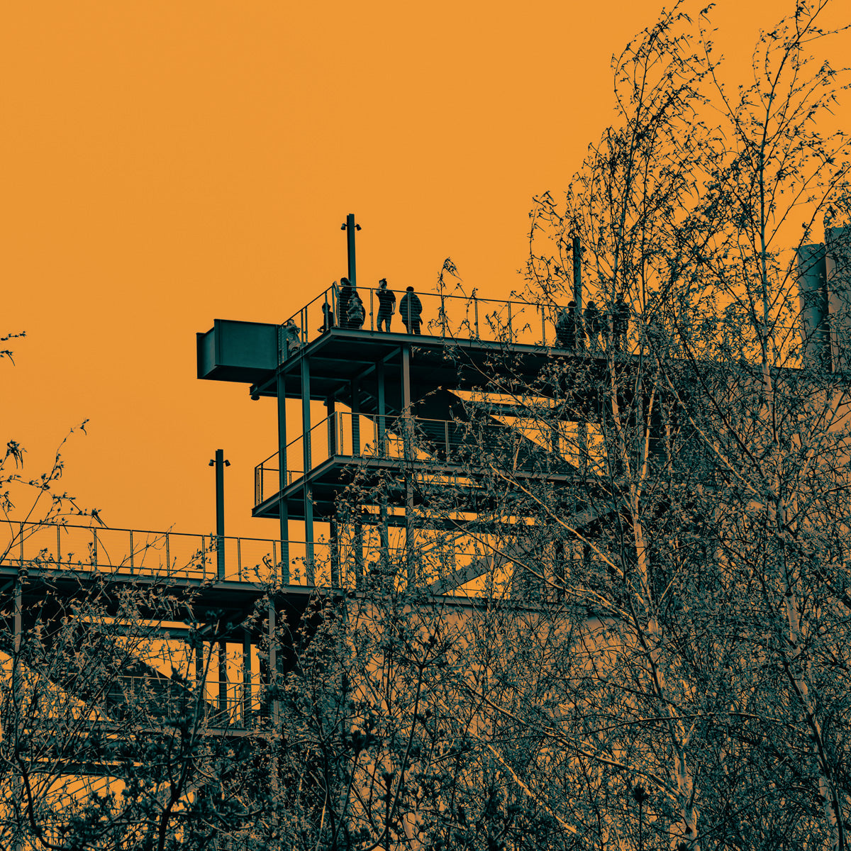 Silhouette of a lookout tower with people on it against an orange sky.