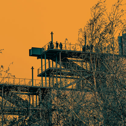 Silhouette of a lookout tower with people on it against an orange sky.